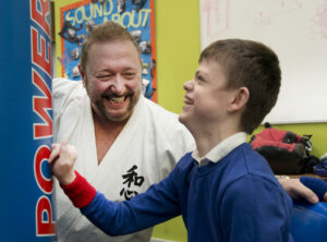 An Ikkaido coach with a young person with a disability laughing with joy and striking a punchbag.